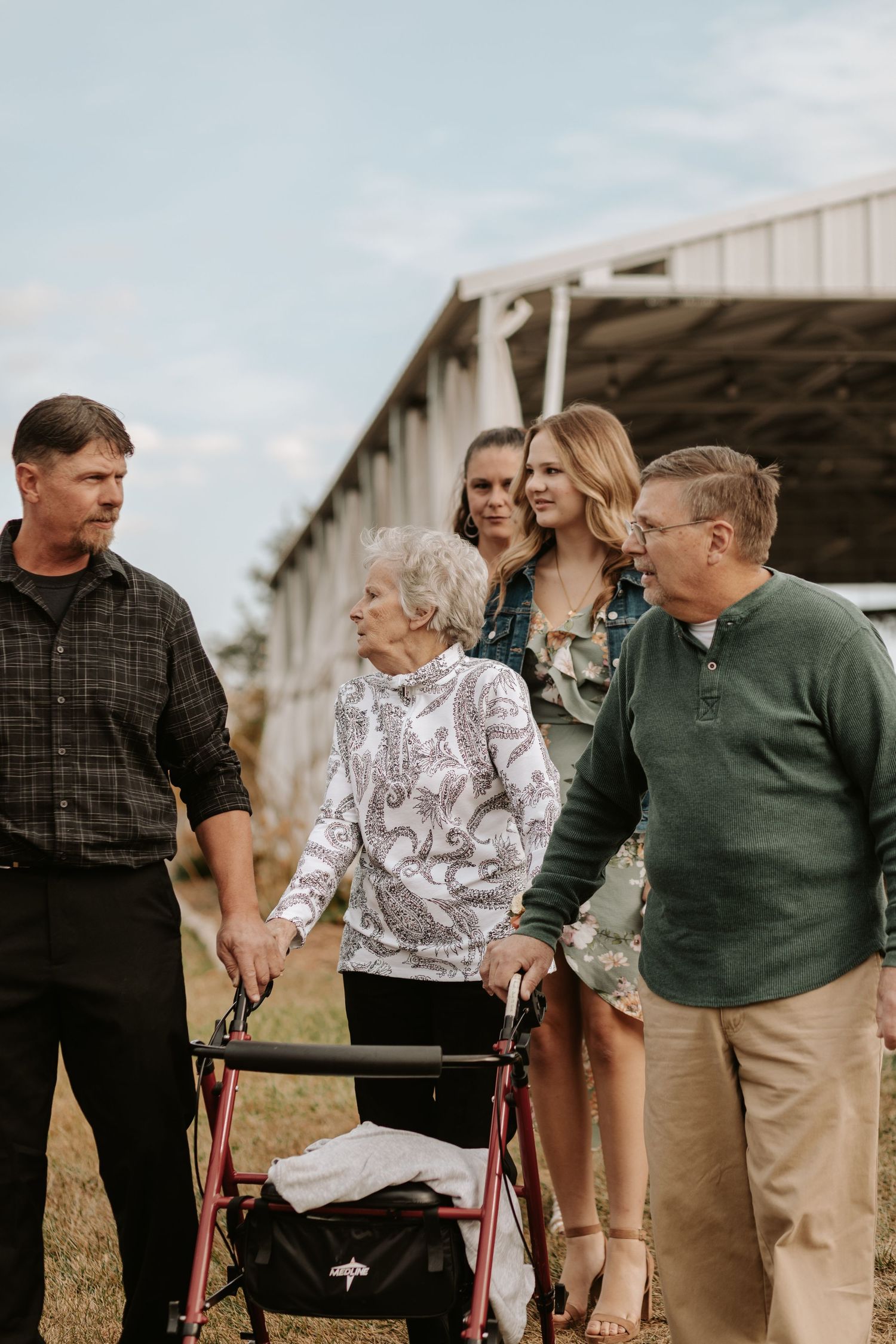 Family members walking together outdoors near farm buildings on sunny day.
