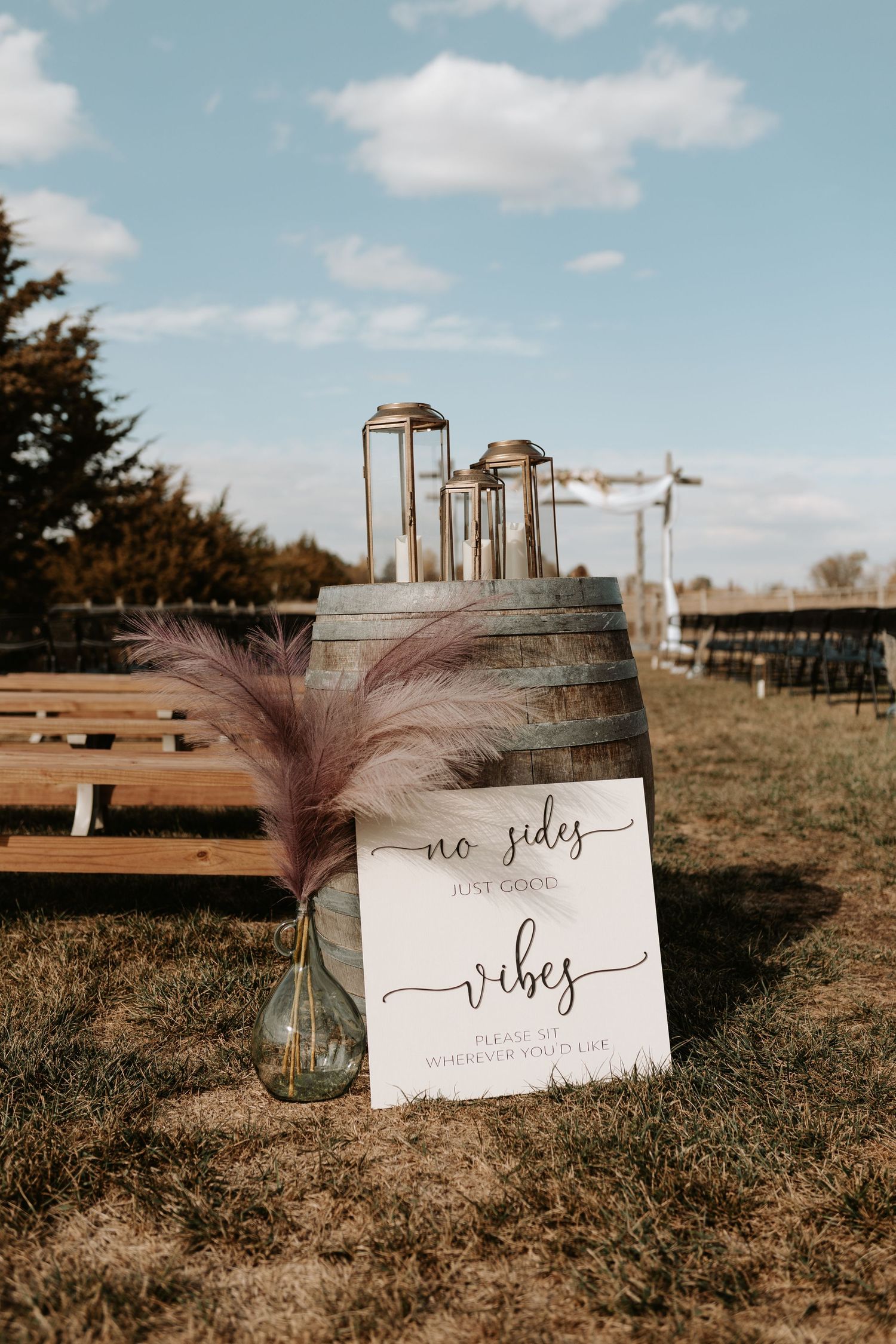 Wedding ceremony seating sign with feather accent against rustic barrel and blue sky.