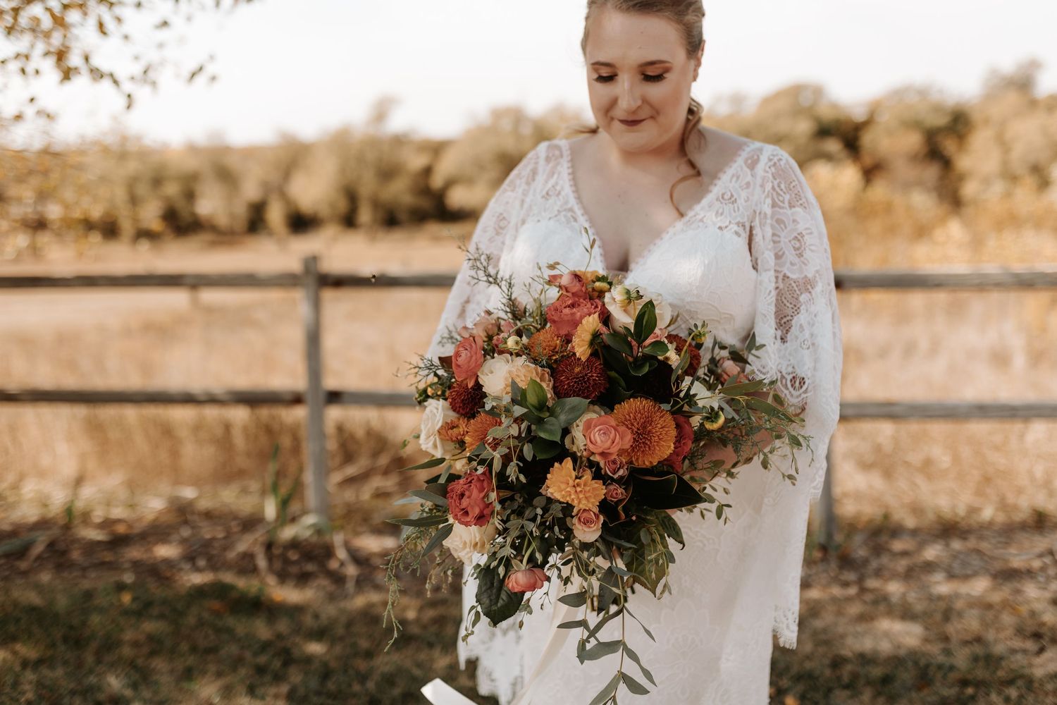 Beautiful bridal bouquet with coral and peach flowers against rustic farm setting.
