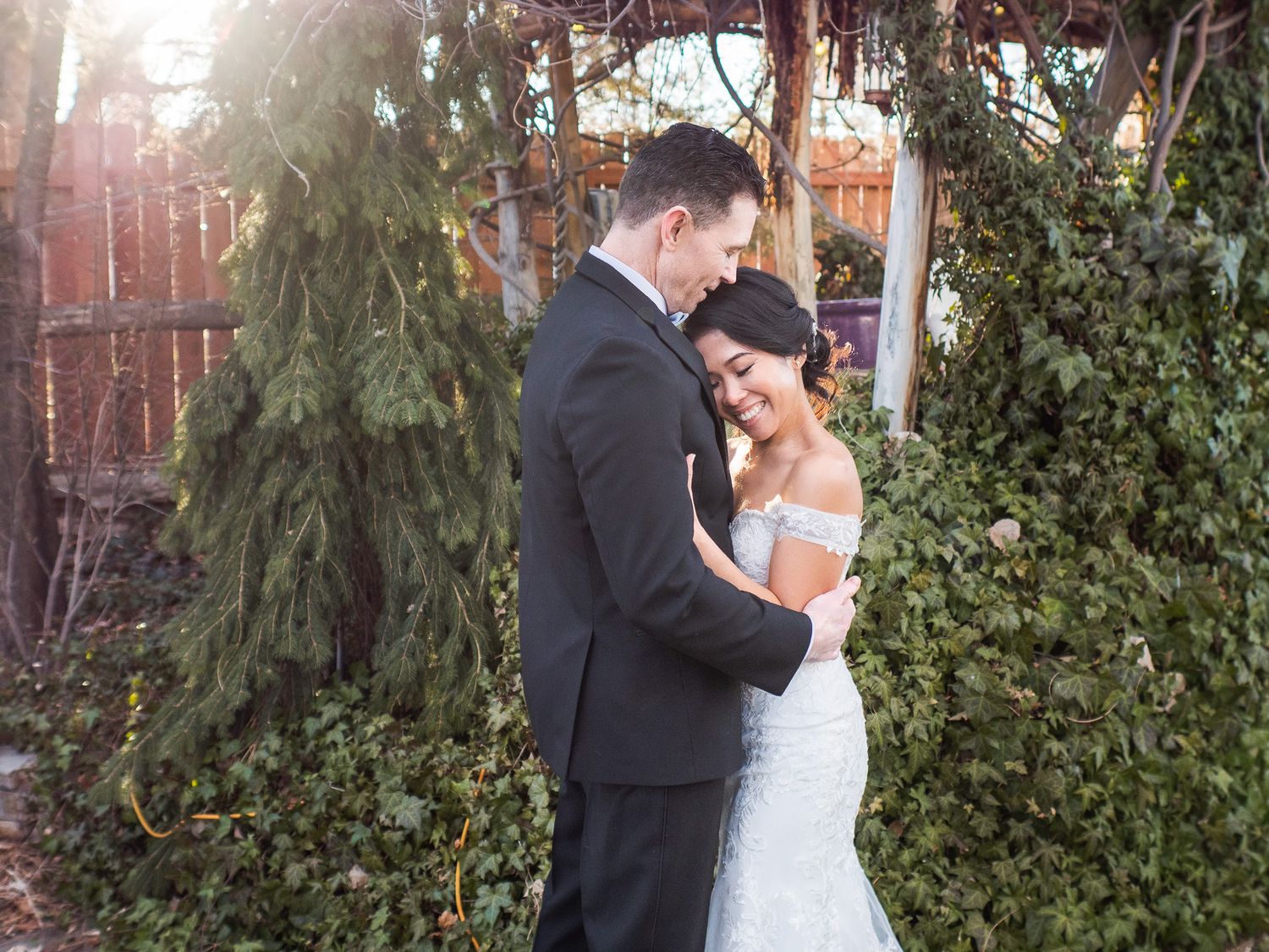 A bride and groom share an intimate moment at Sierra Water Gardens in a garden with evergreen trees and sunset lighting.