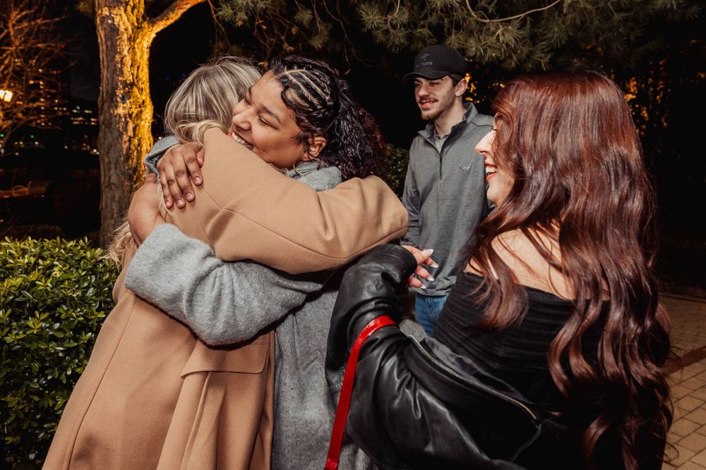 Group sharing hugs and celebrations in an outdoor garden setting at night.