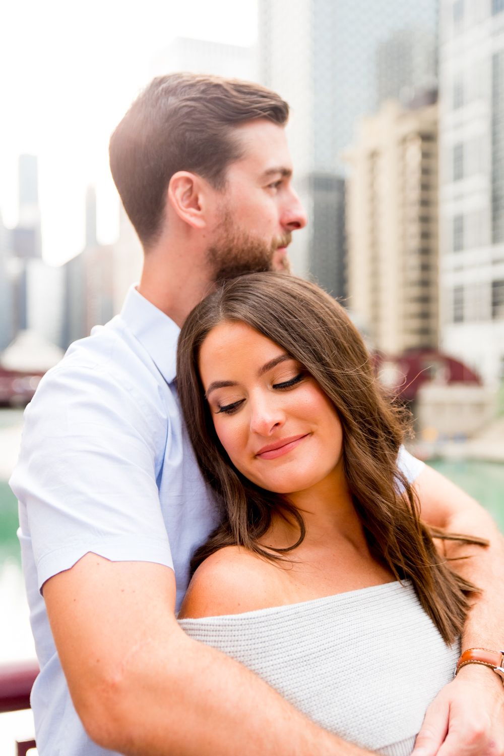 man with brown hair hugging fiance from behind, looking at the Chicago River for sunrise engagement pictures in Chicago