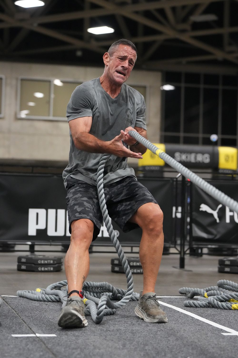 Athlete performing intense rope training exercise in a gym with Hyrox equipment.
