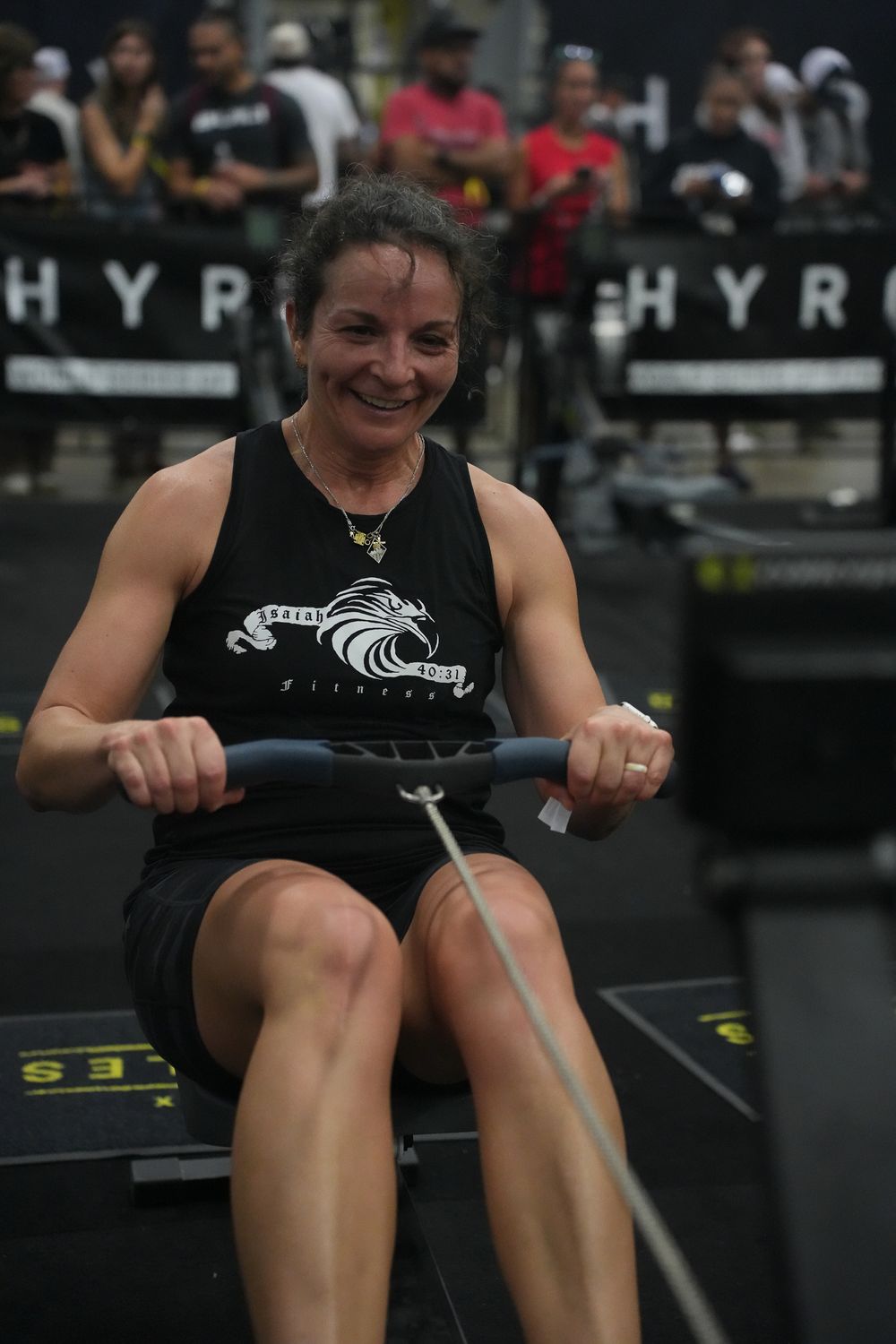 Athlete smiling while competing on rowing machine at indoor sports event.