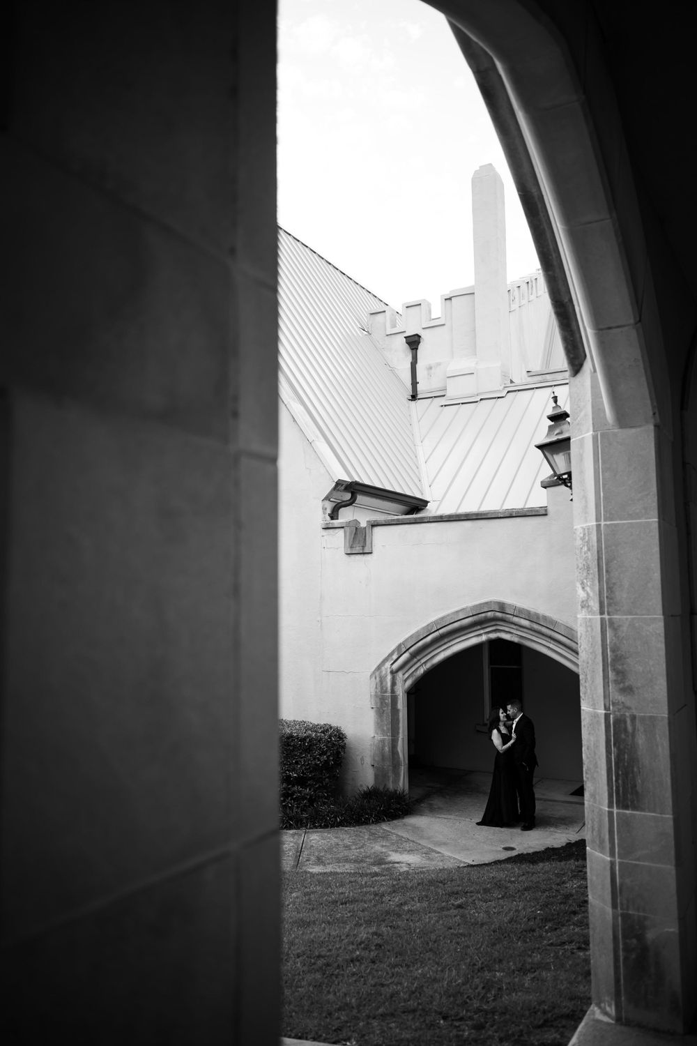 Black and white architectural photo frames figure through gothic stone archway.