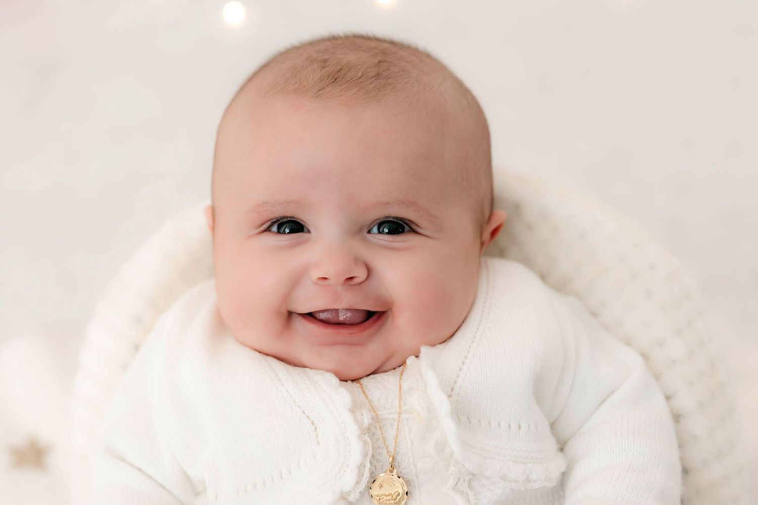 Fotografía de una bebé de tres meses sonriendo en su sesión de bautizo en estudio.