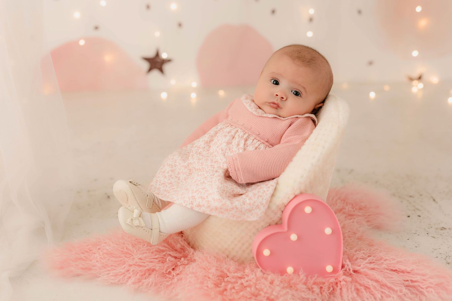 Fotografía de una bebé de tres meses sentada en sillón blanco en su sesión de seguimiento en estudio.