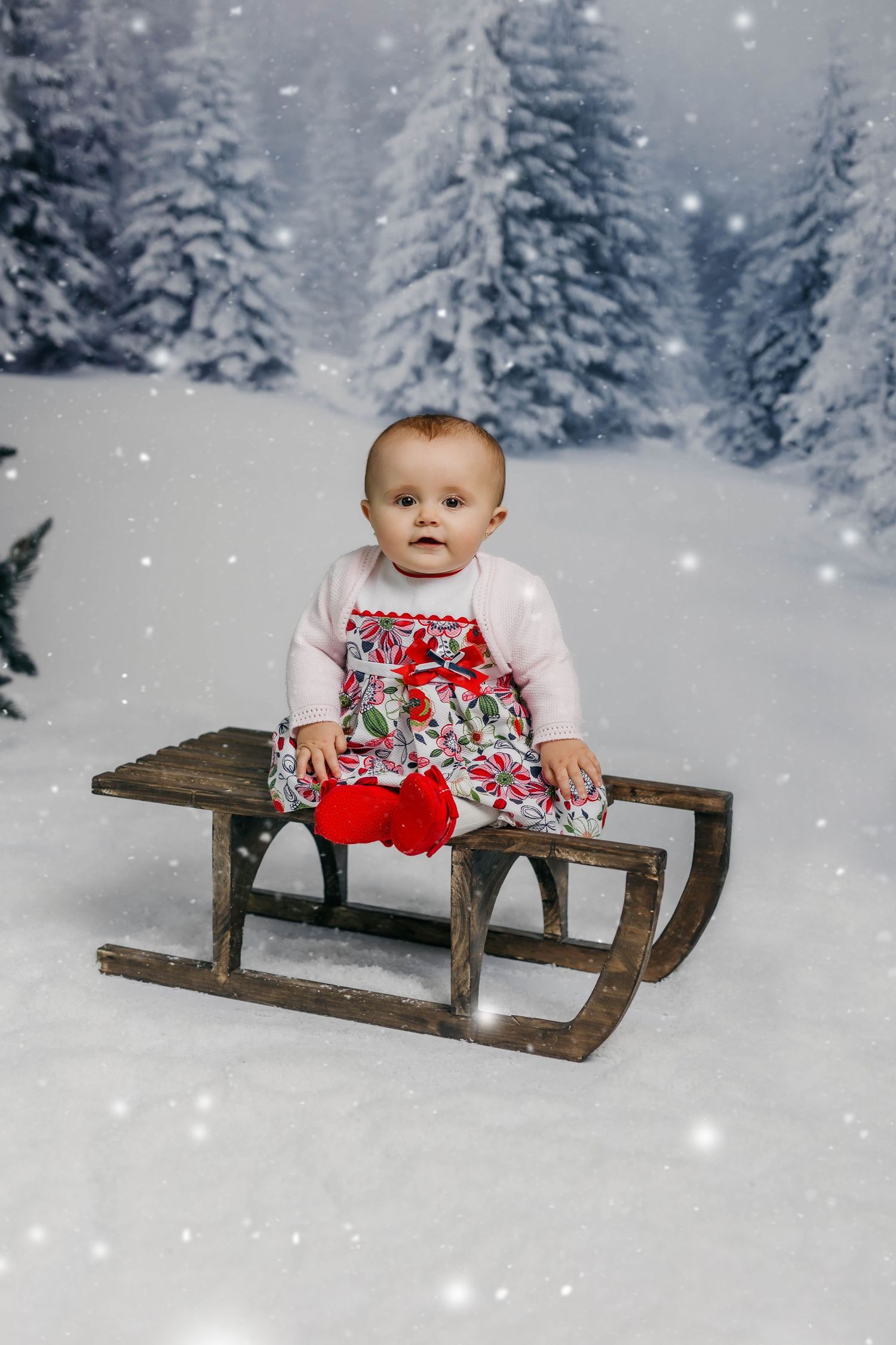 Foto de bebé de nueve meses en sesión navideña sentada en un trineo con nieve.
