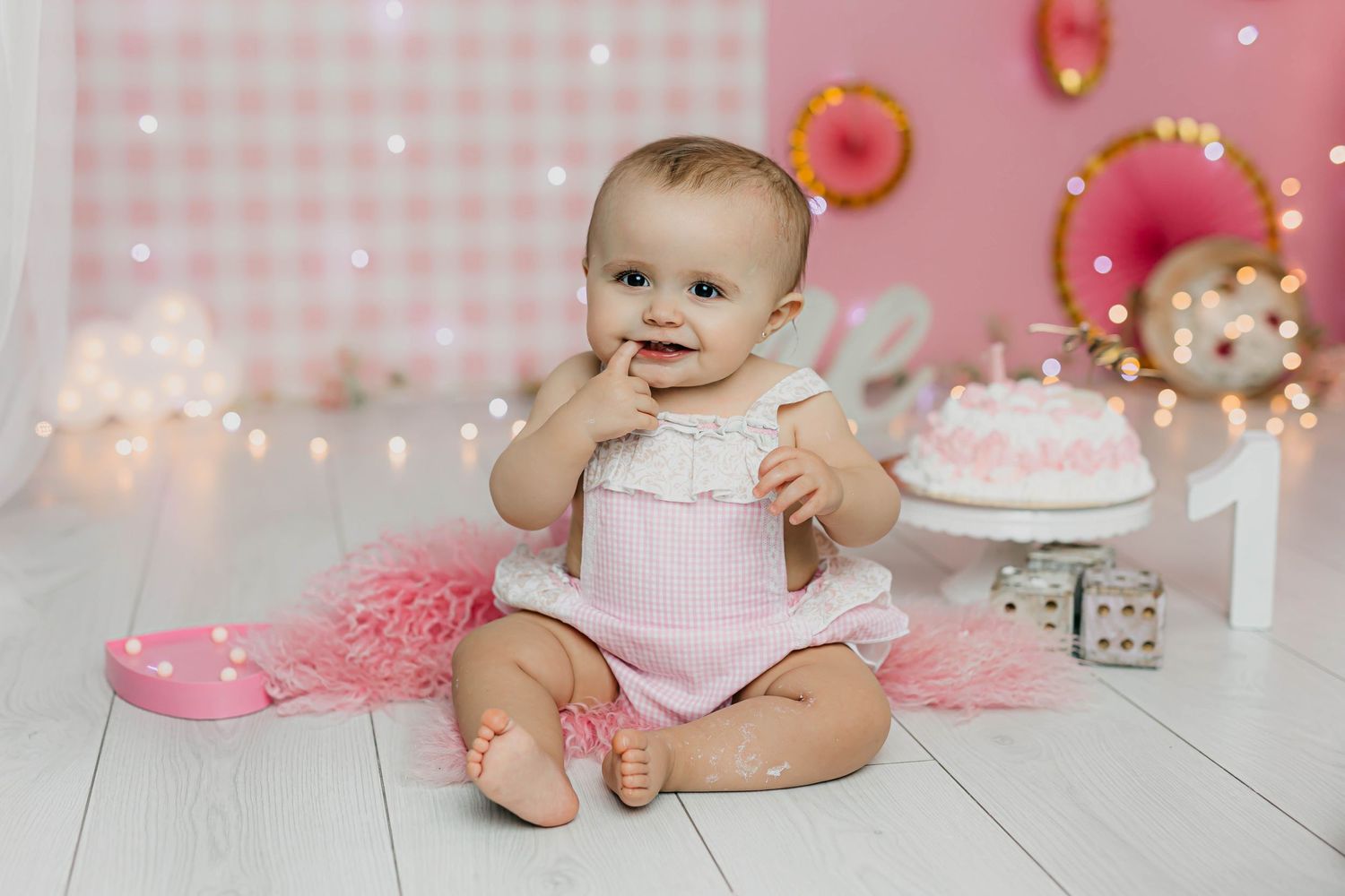 Retrato del primer añito de una niña con tarta, y vestimenta en cuadros vichy rosas y decoración en tonos rosas.
