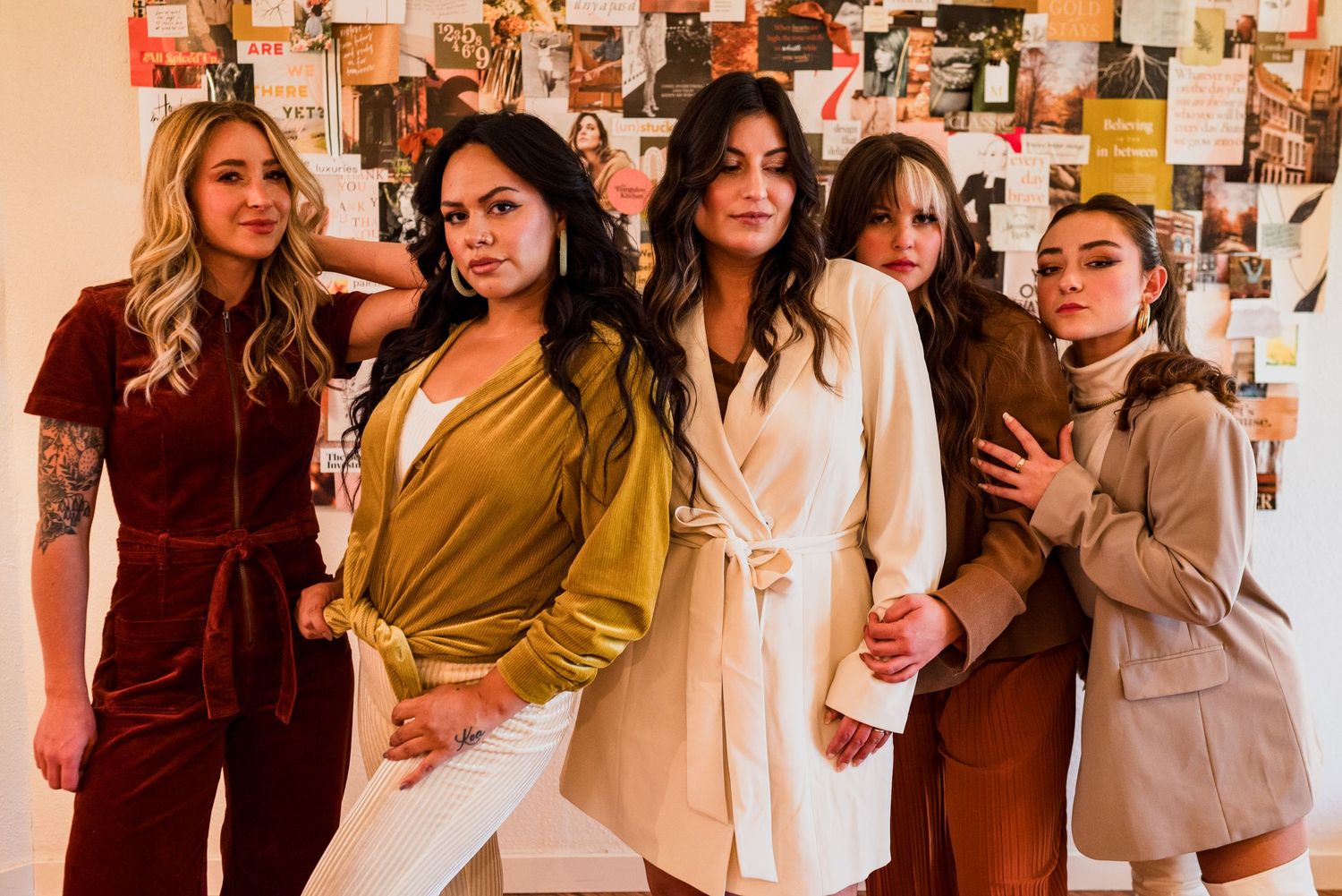 Group poses together in autumn tones wearing stylish blazers and coats against a wall with photos.