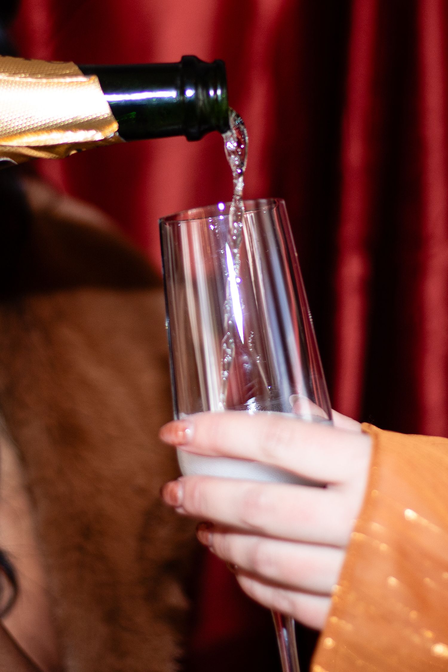 Champagne being poured into a glass against a red curtain backdrop.