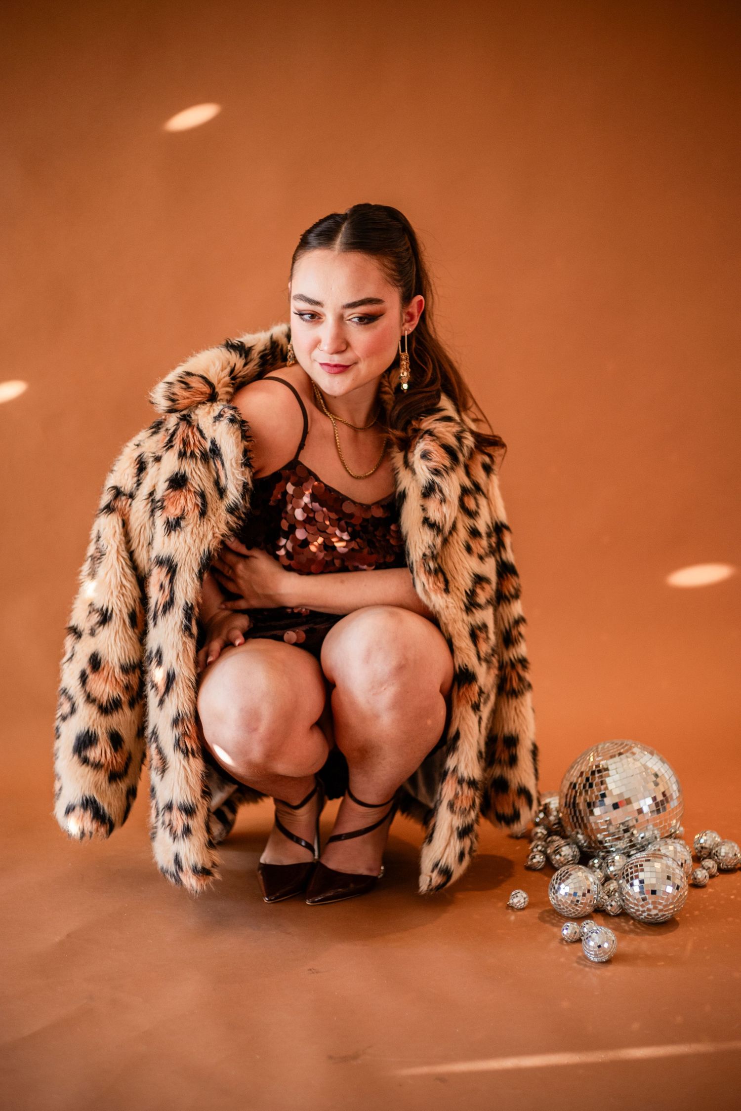 Fashion photoshoot with leopard print coat and festive decorations on orange background.
