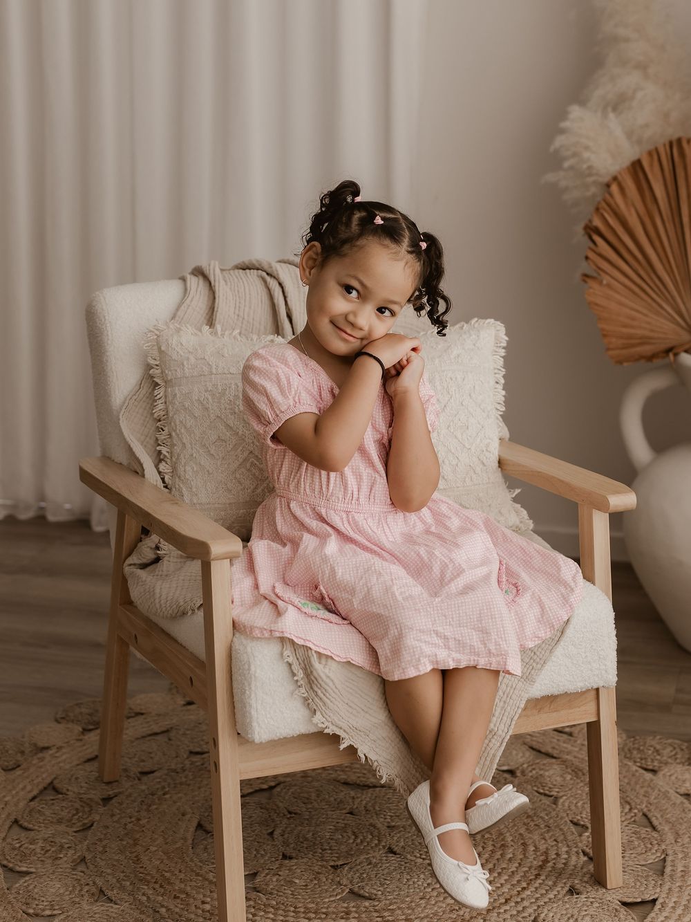 Charming portrait in a pink dress and white shoes against neutral decor.