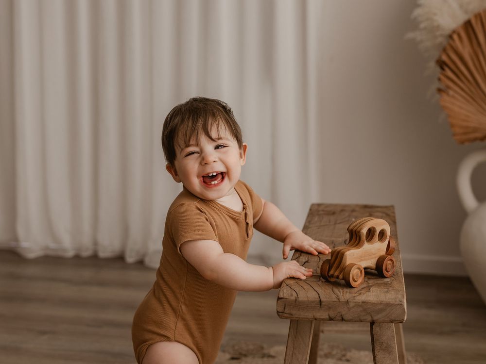 Joyful moment playing with wooden toy on small stool in natural-toned setting.