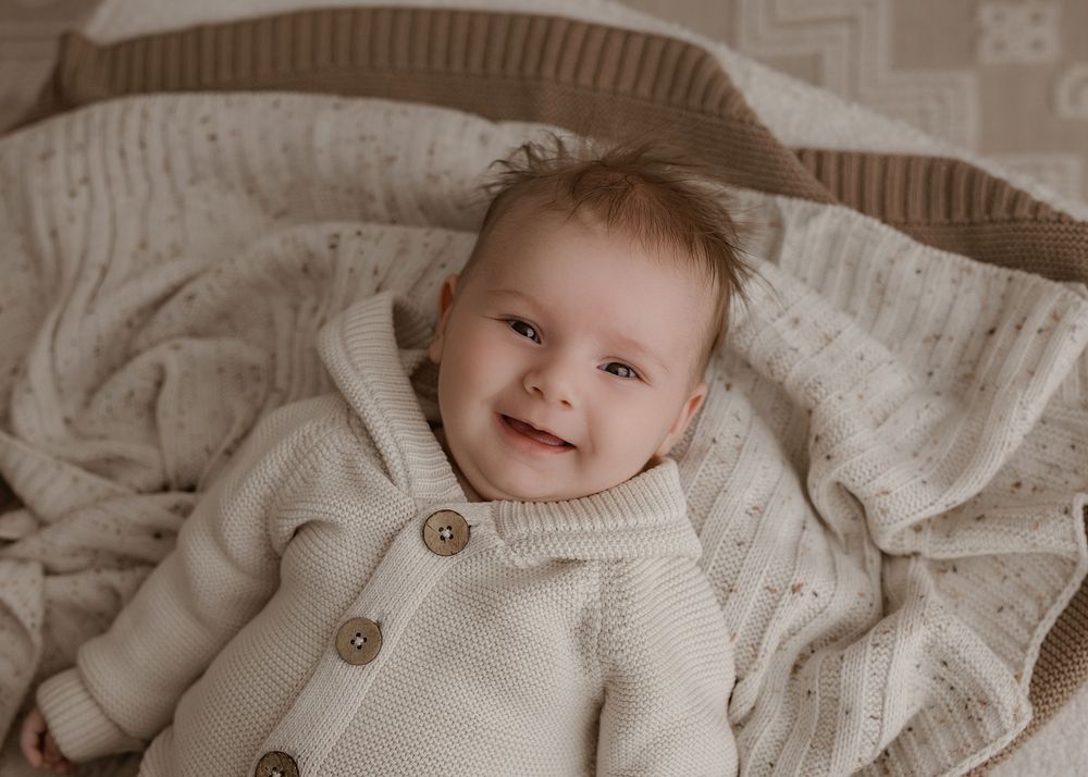 A cozy collage of a baby wearing a cream knit sweater with wooden buttons shown from different angles.