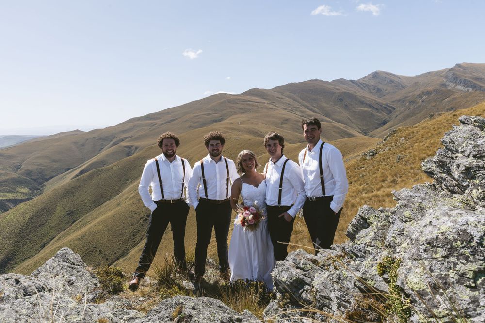 Wedding party in formal attire poses on rocky mountain outcrop.