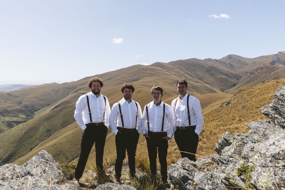 Group poses in white shirts and suspenders against mountainous landscape.