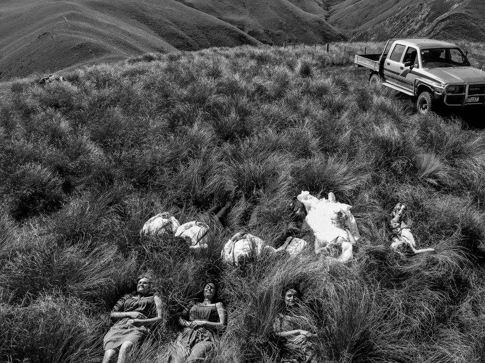 Black and white photo of wedding party resting in mountain grass near parked truck.