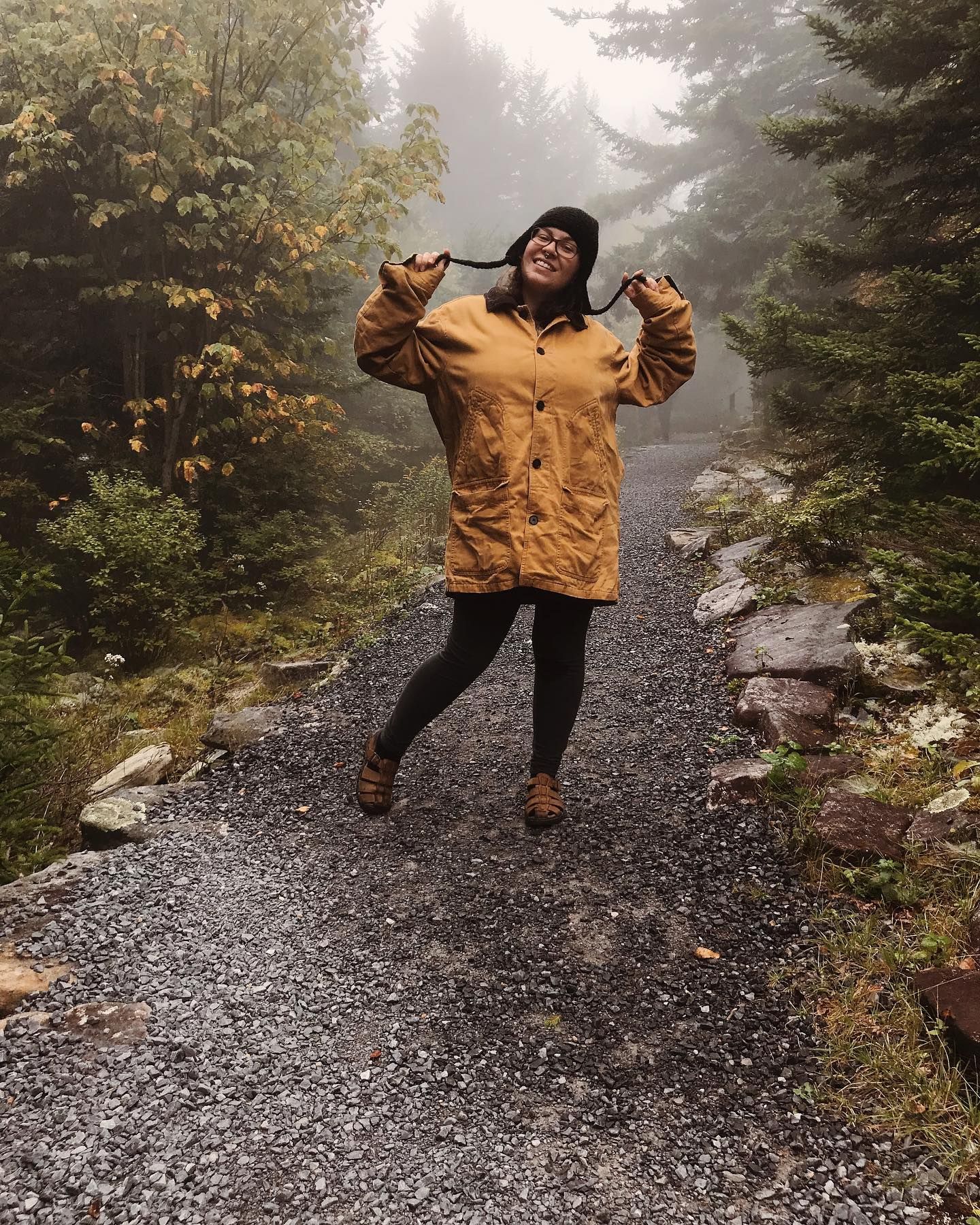 Anne Kirk in brown jacket poses playfully on foggy mountain trail.
