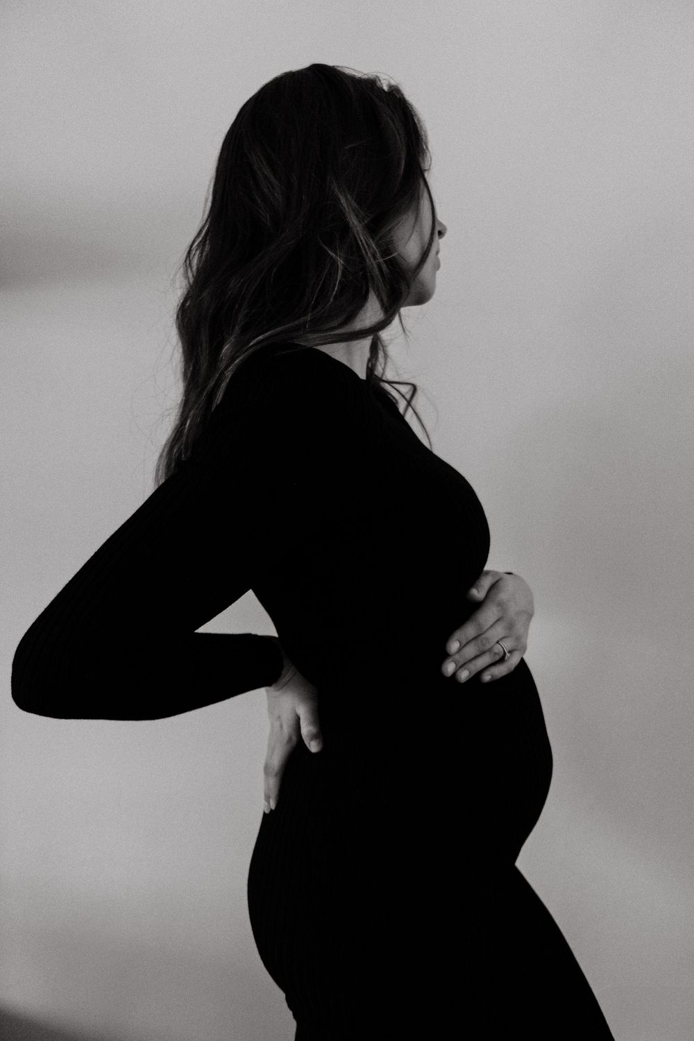 Silhouette profile portrait with elegant black attire highlighting a pregnancy bump in black and white photography.
