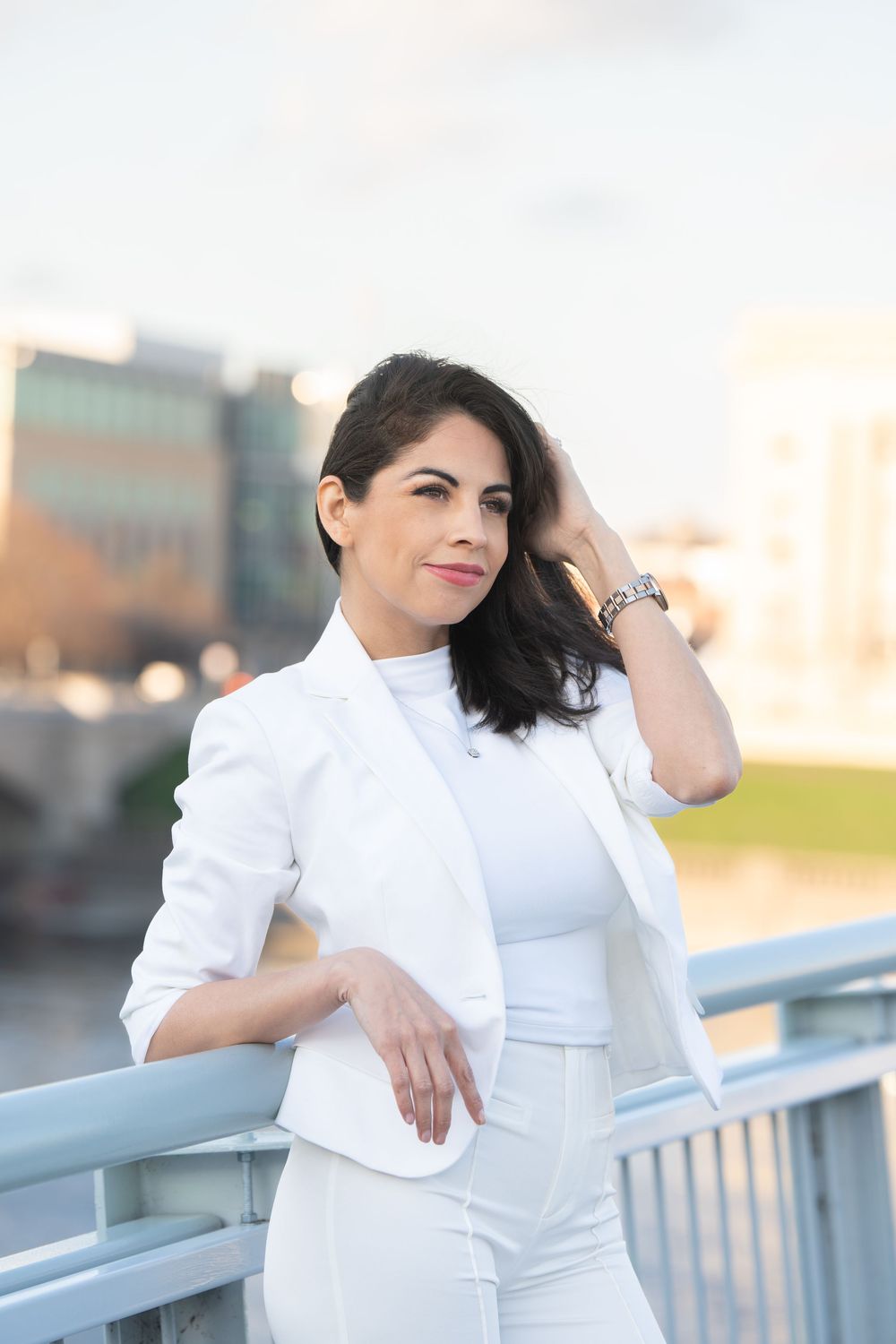 Someone in an elegant white outfit poses confidently on a bridge during sunset.