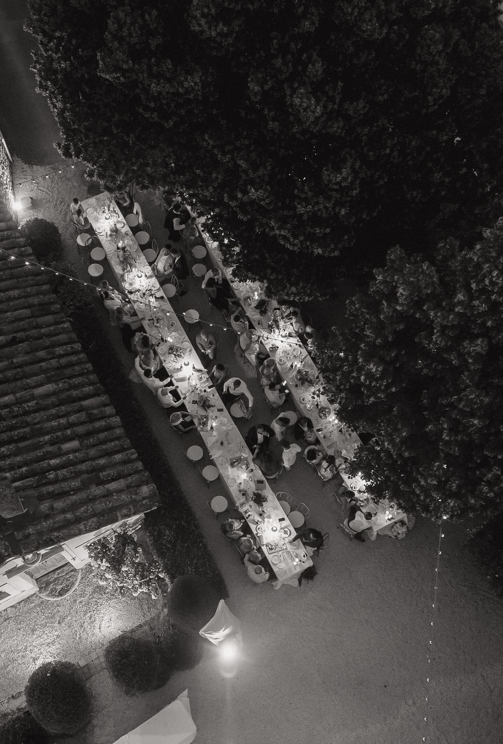 Aerial black and white view of long dining tables set up outdoors with string lights creating an elegant dinner atmosphere.
