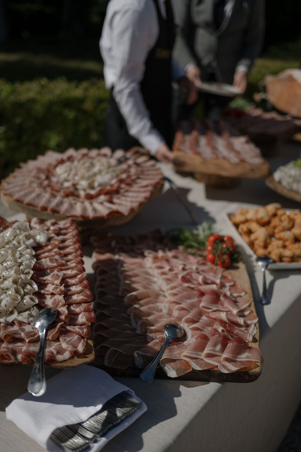 Charcuterie board with artfully arranged meats and appetizers being set up at an outdoor catering event.