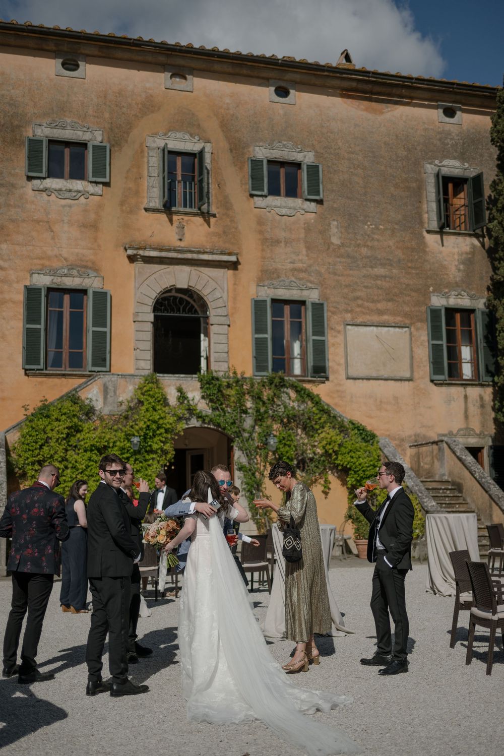 Wedding ceremony participants gather outside a historic Mediterranean stone building under blue skies.
