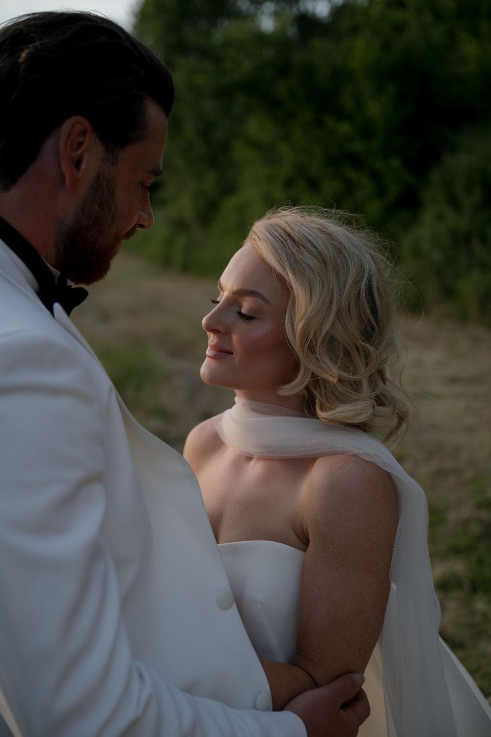 Intimate wedding portraits shot at dusk show couple in white attire sharing tender moments together.