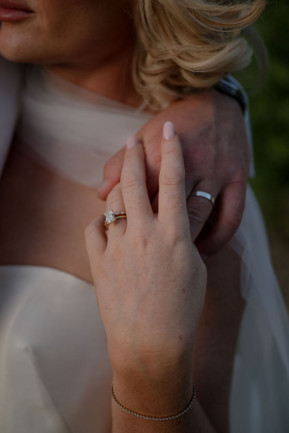 Close-up shots of sparkling engagement ring on hand against pastel formal attire in soft natural lighting.
