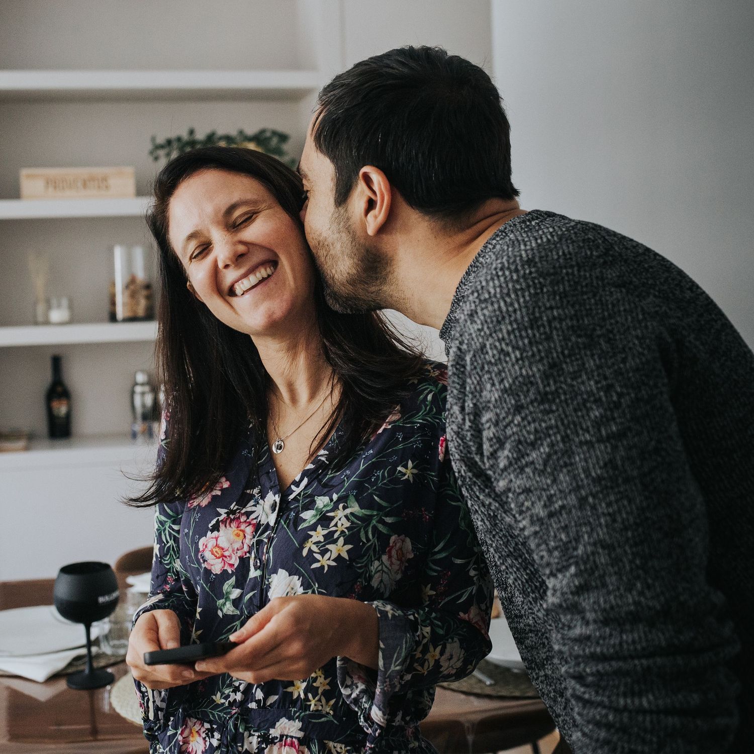 sesiones fotográfica de pareja en casa y relaxados. montecarmelo. ella con el movil en las manos y el roba un beso.