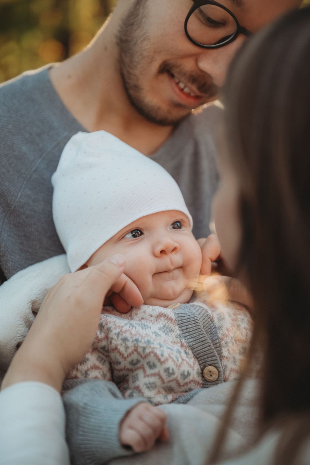 A sweet moment as parents cradle their baby wearing a white hat and patterned sweater.