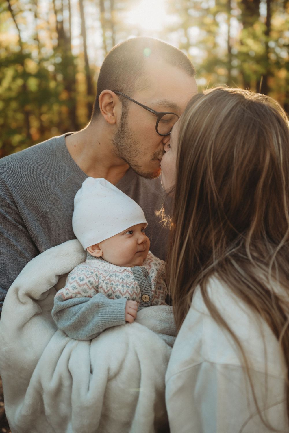 An intimate family moment shared between parents and their baby in golden forest light.
