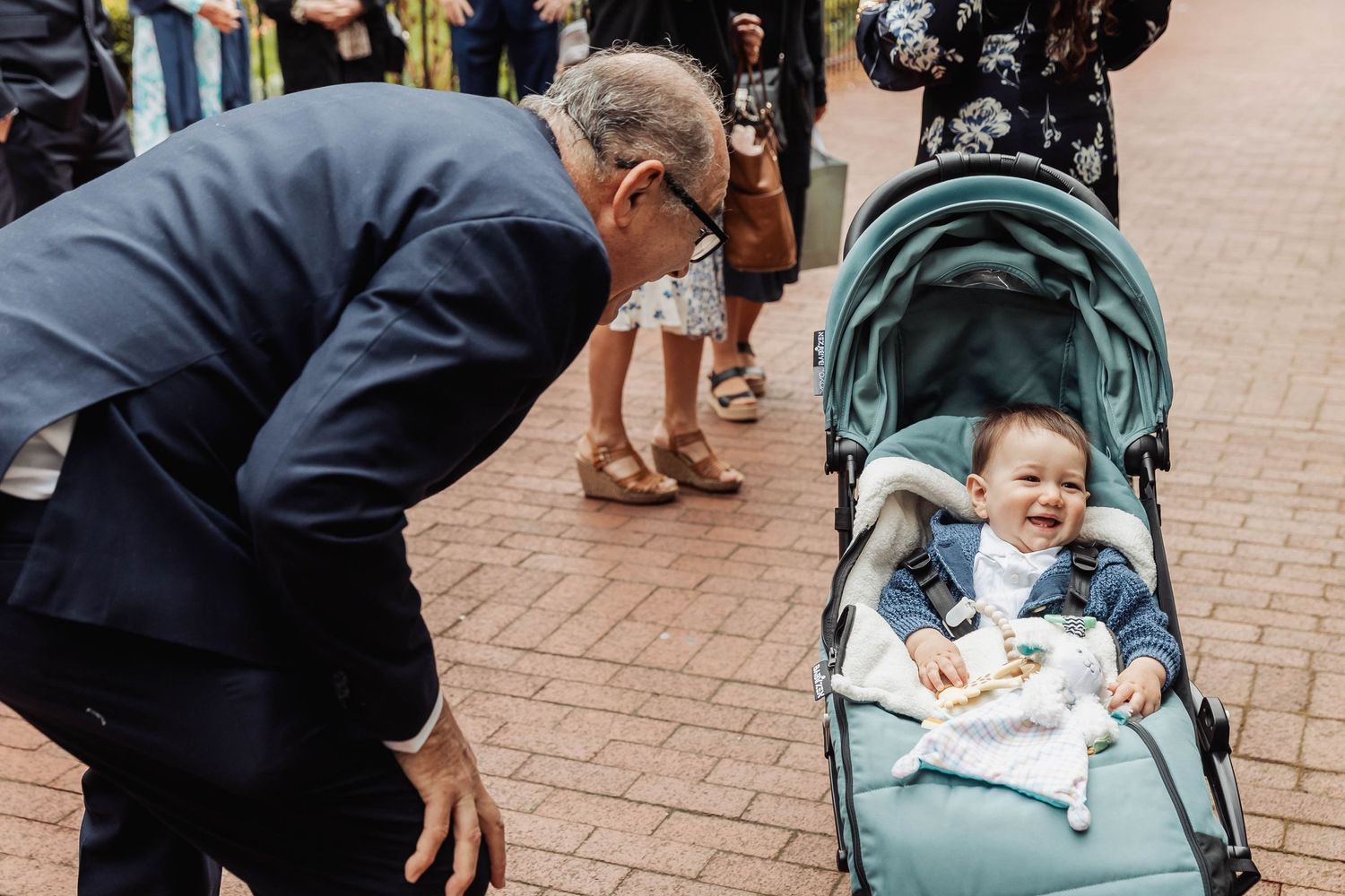 A heartwarming interaction between an adult and baby in a stroller on brick pavement.