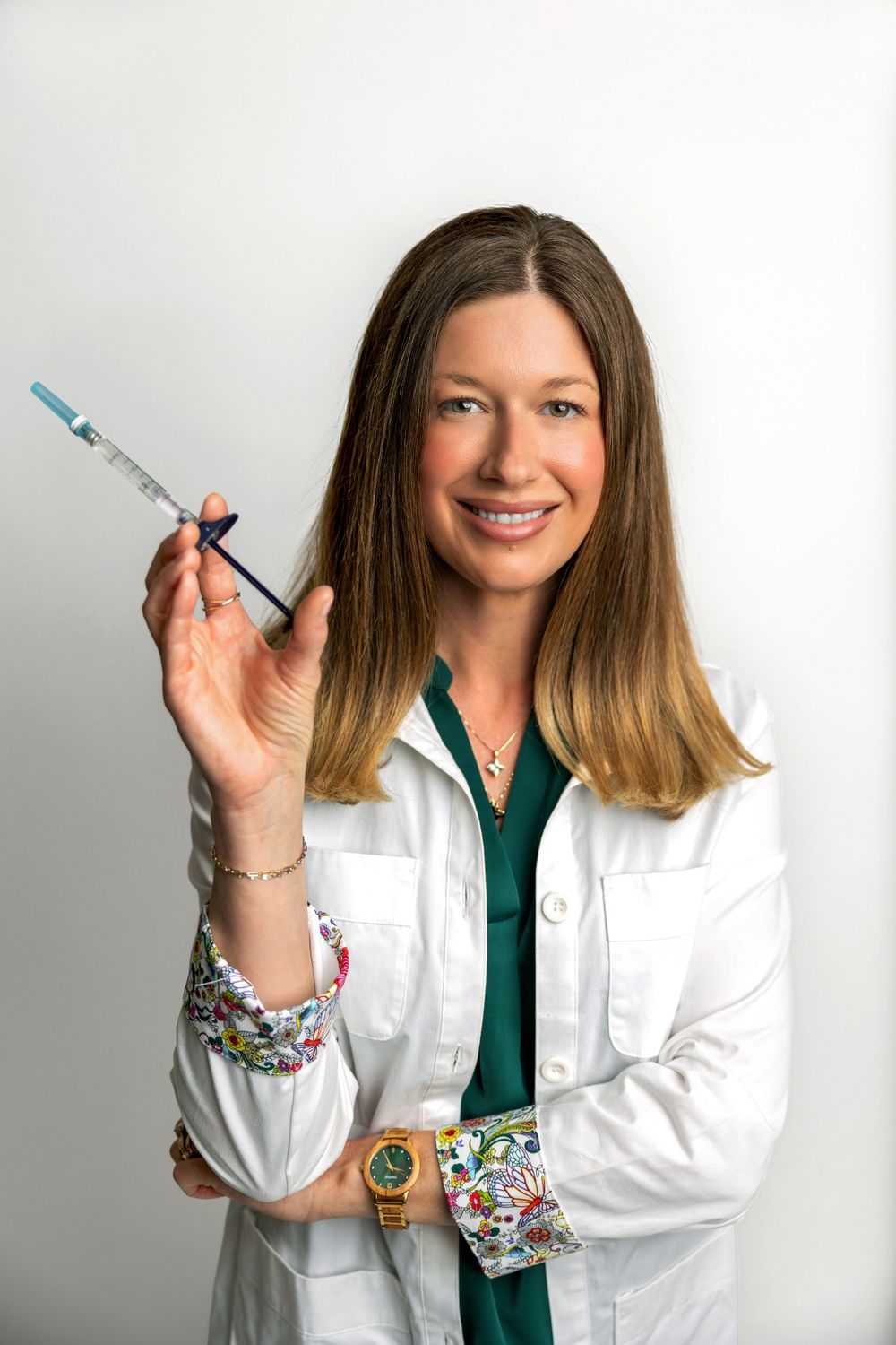 Healthcare provider in white coat holds dental syringe while wearing colorful patterned sleeves.