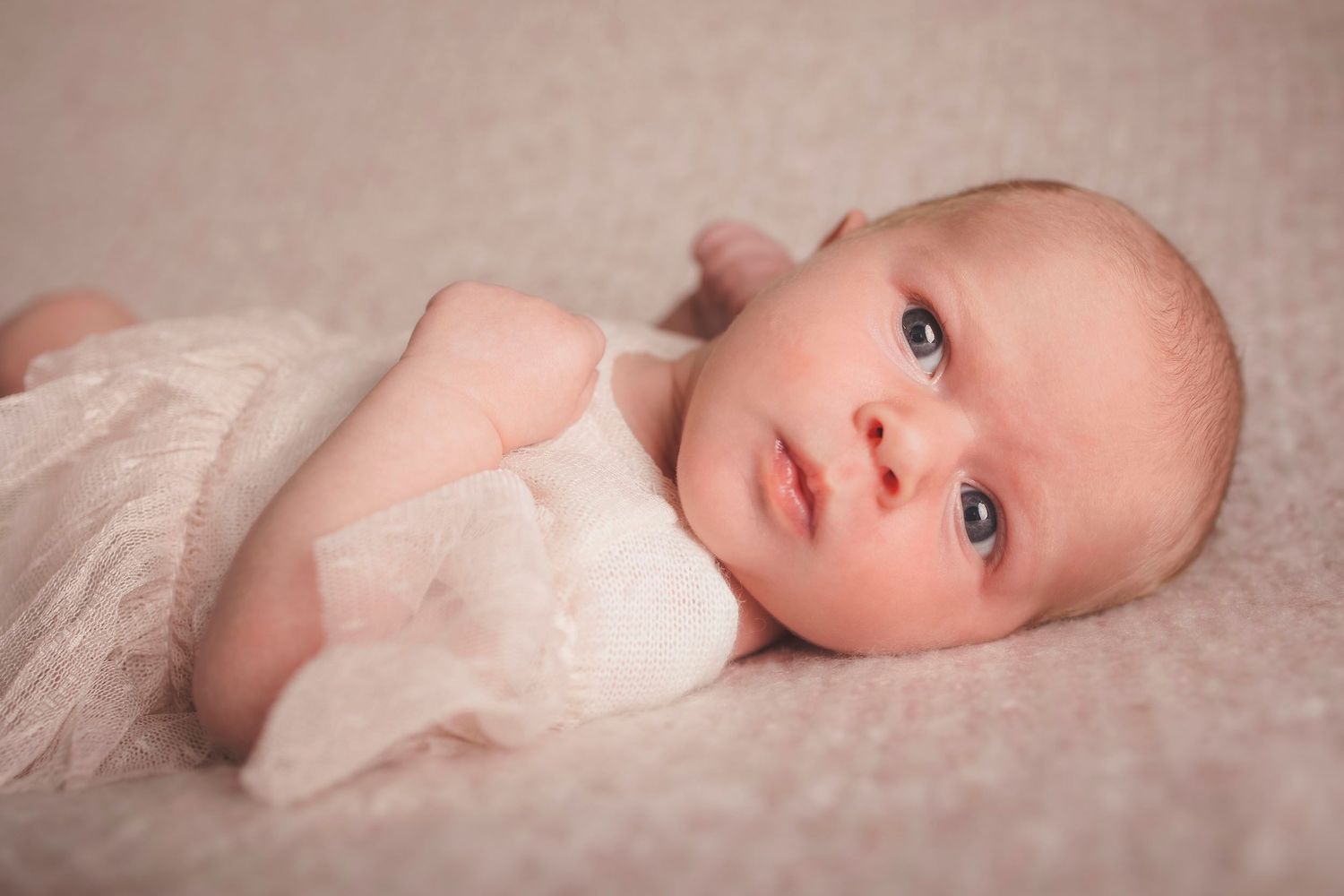 A newborn baby wrapped in delicate white fabric lying on soft pink surface. Tiny moments newborn photography in Fareham & Gosport studio
