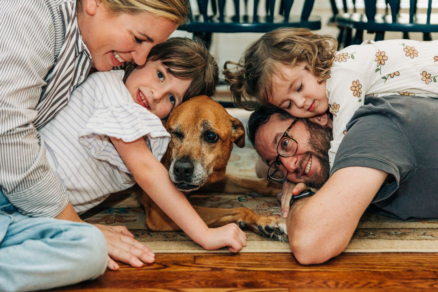 A dog and family lying together on hardwood floor at home in series of candid lifestyle moments.