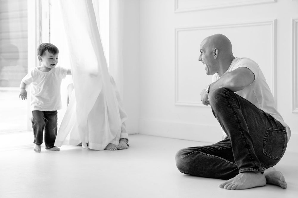 Black and white photo of father and toddler interacting in light-filled white room.