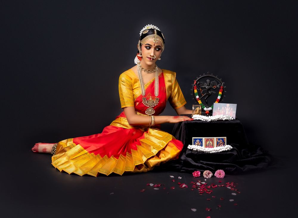 Classical Indian dancer in vibrant yellow and red costume poses elegantly with birthday cake and decorative elements.