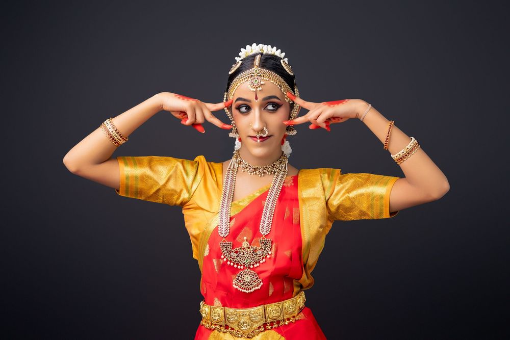 Traditional dancer performs expressive hand gestures in colorful costume against dark background.