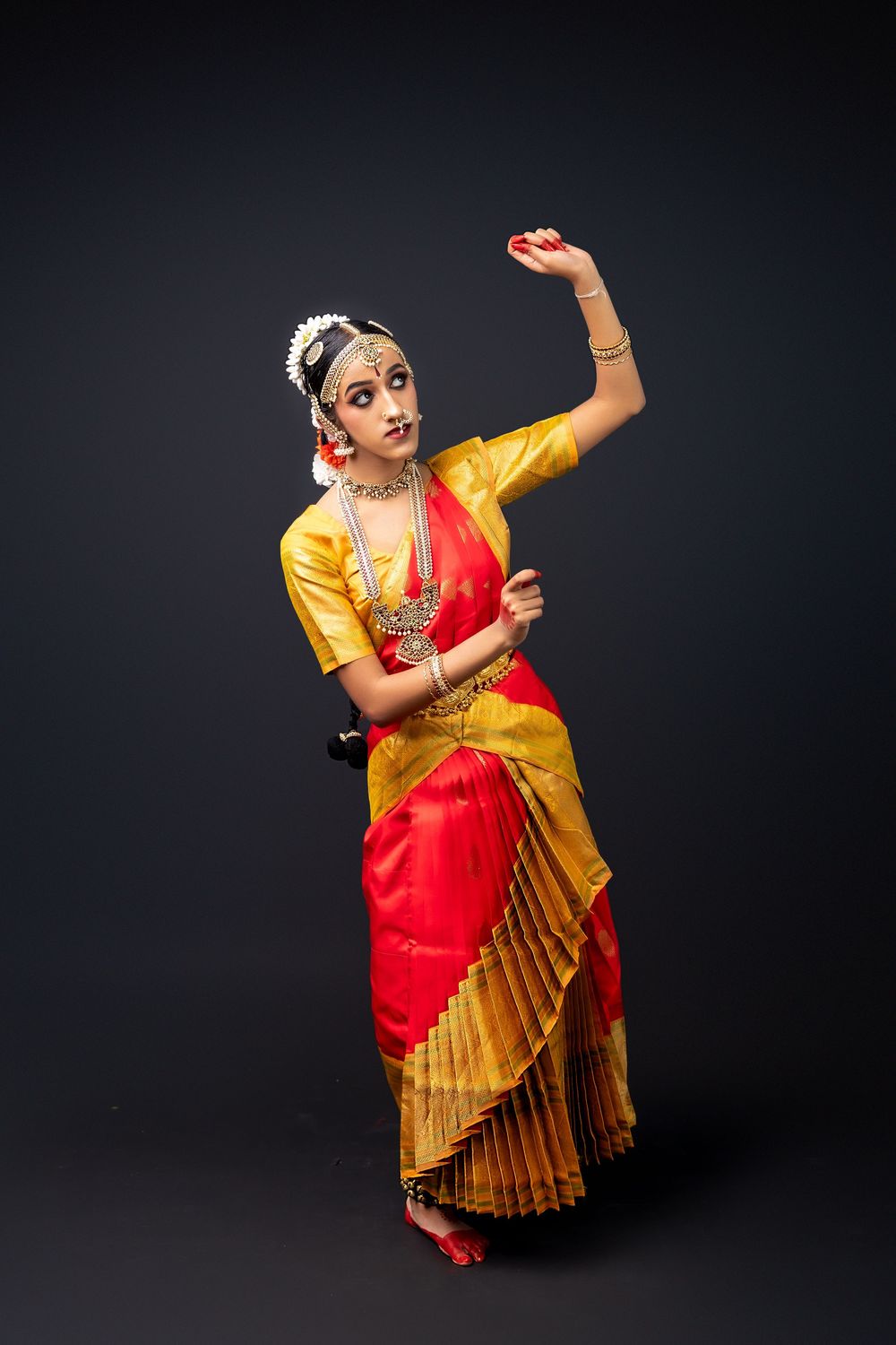 Bharatanatyam dancer strikes expressive poses wearing vibrant red and gold sari in studio photoshoot.