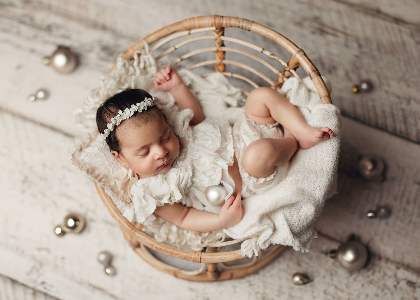 A baby sleeps curled up on a tiny bamboo chair surrounded by silver Christmas ornaments. Elizabeth Lang Photography