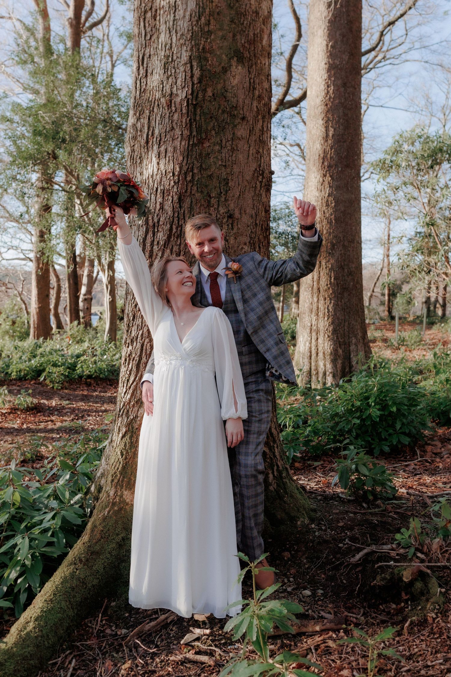 A couple shares a joyful moment among tall trees in a forest setting.