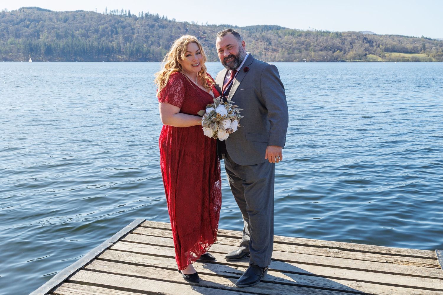 A romantic proposal scene unfolds on a lakeside dock with mountains in the background.