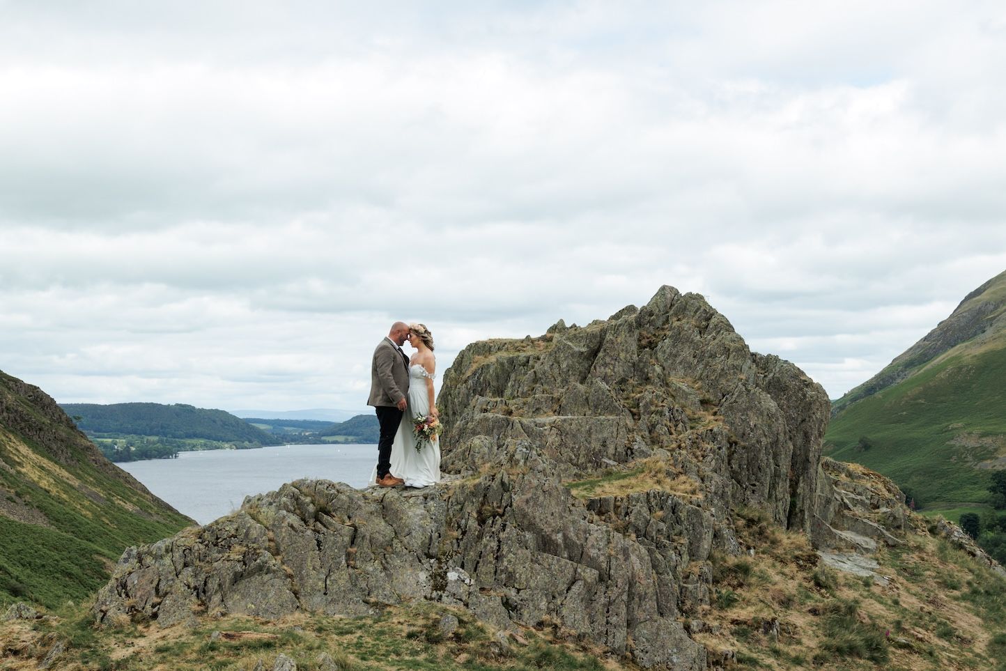 A dramatic panoramic view of rugged mountain peaks and ridges in the Lake District under cloudy skies.