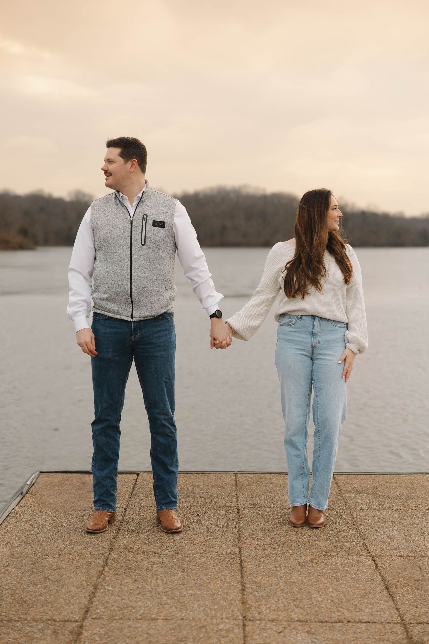 Couple playfully walking and interacting on a waterfront path wearing casual clothing.