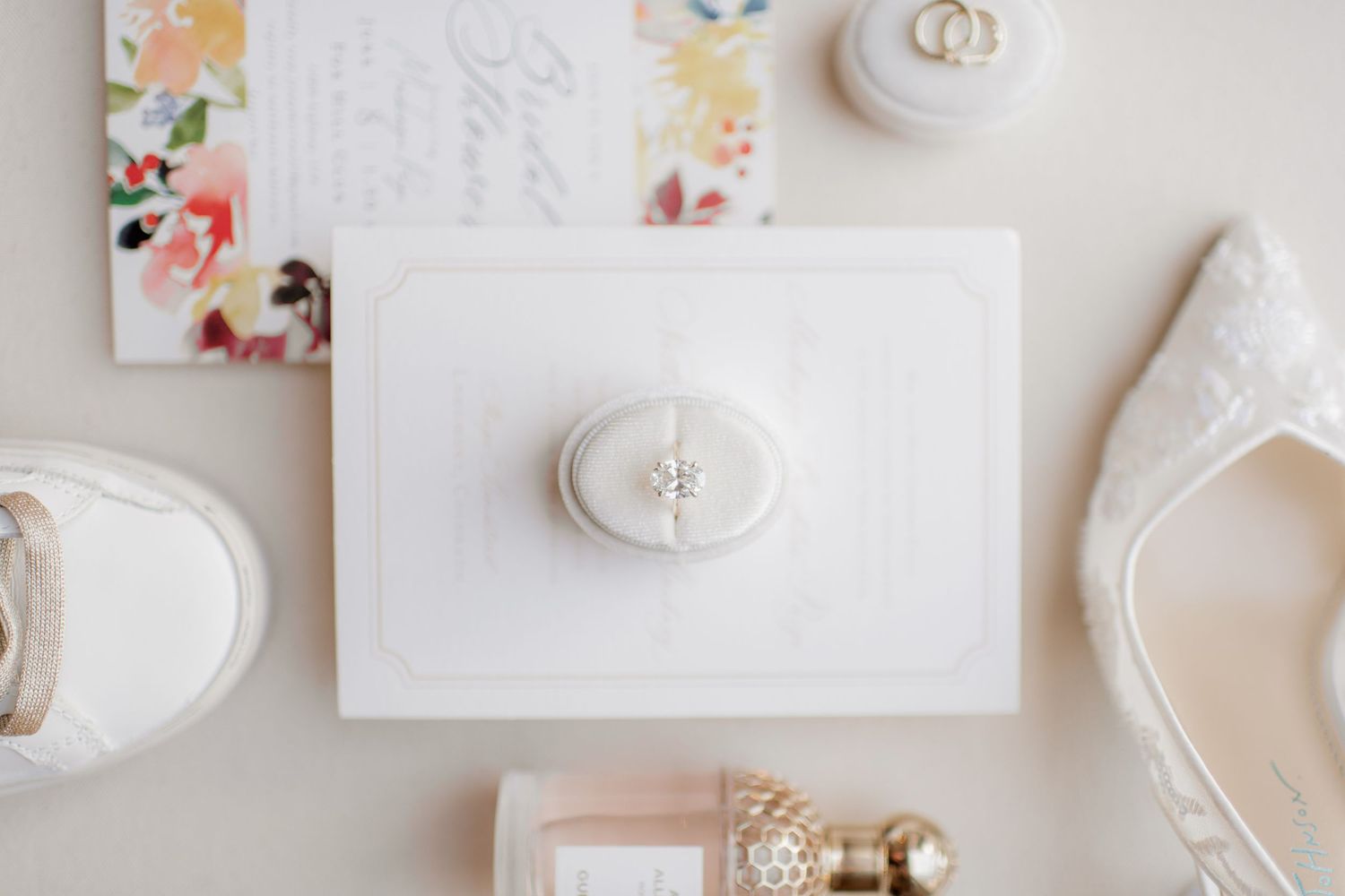 A bride in a flowing white wedding dress with long train sits gracefully on hardwood floor in bright minimalist room.