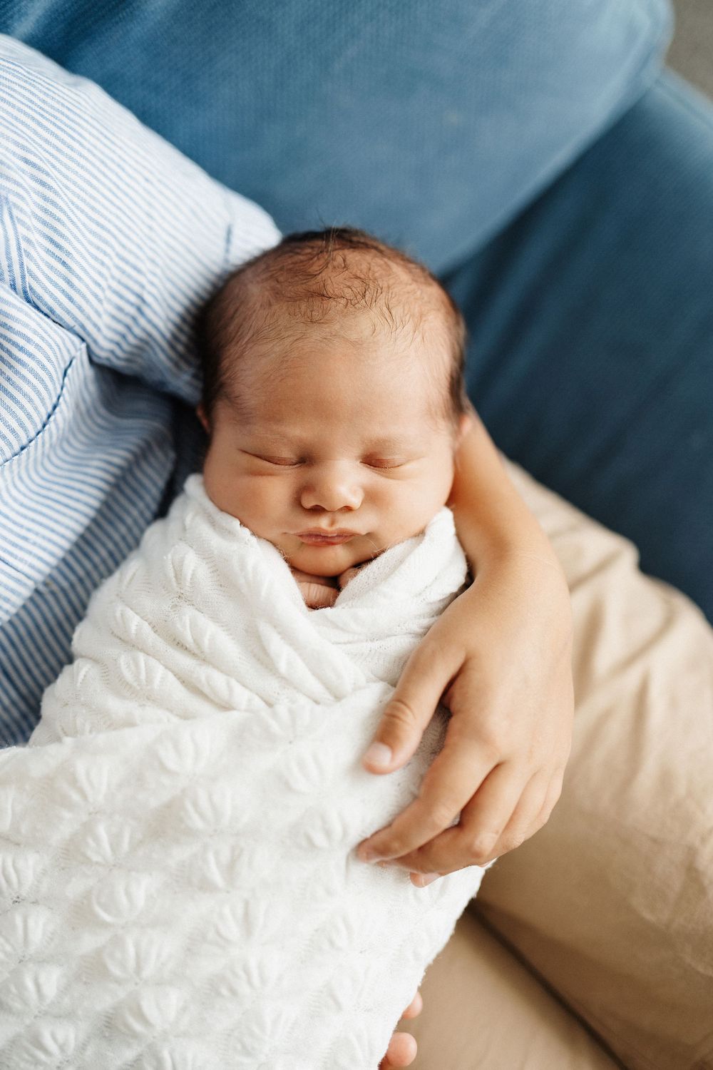 A sleeping newborn baby wrapped in white blanket resting peacefully against a blue background.