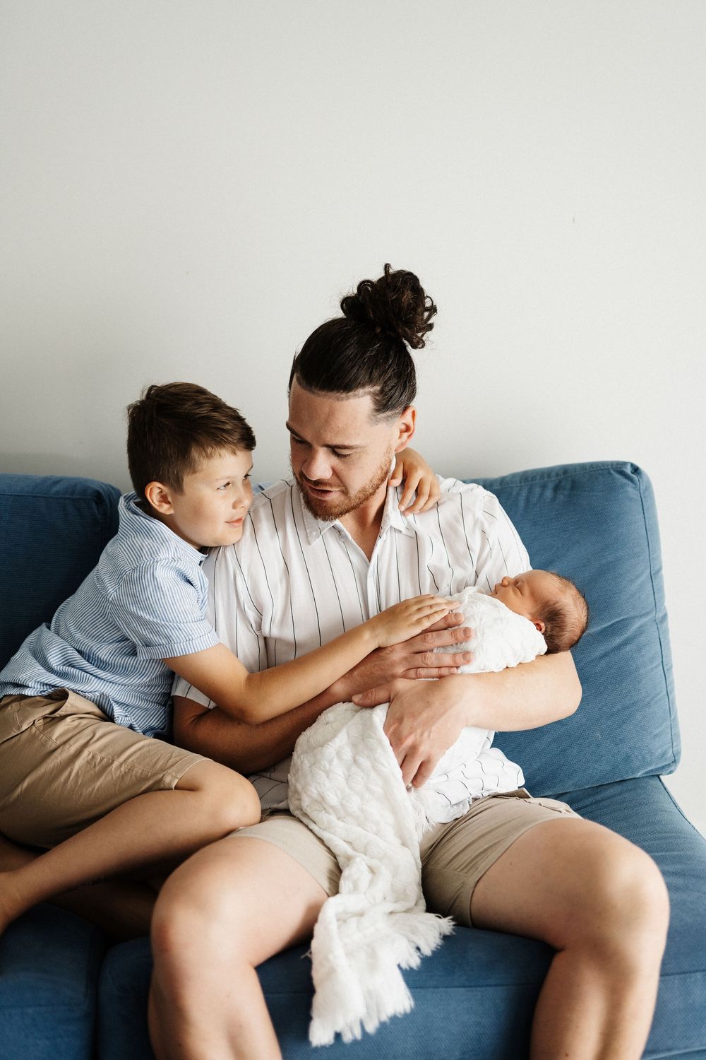 Intimate family gathering on a blue couch with two siblings meeting their new baby.