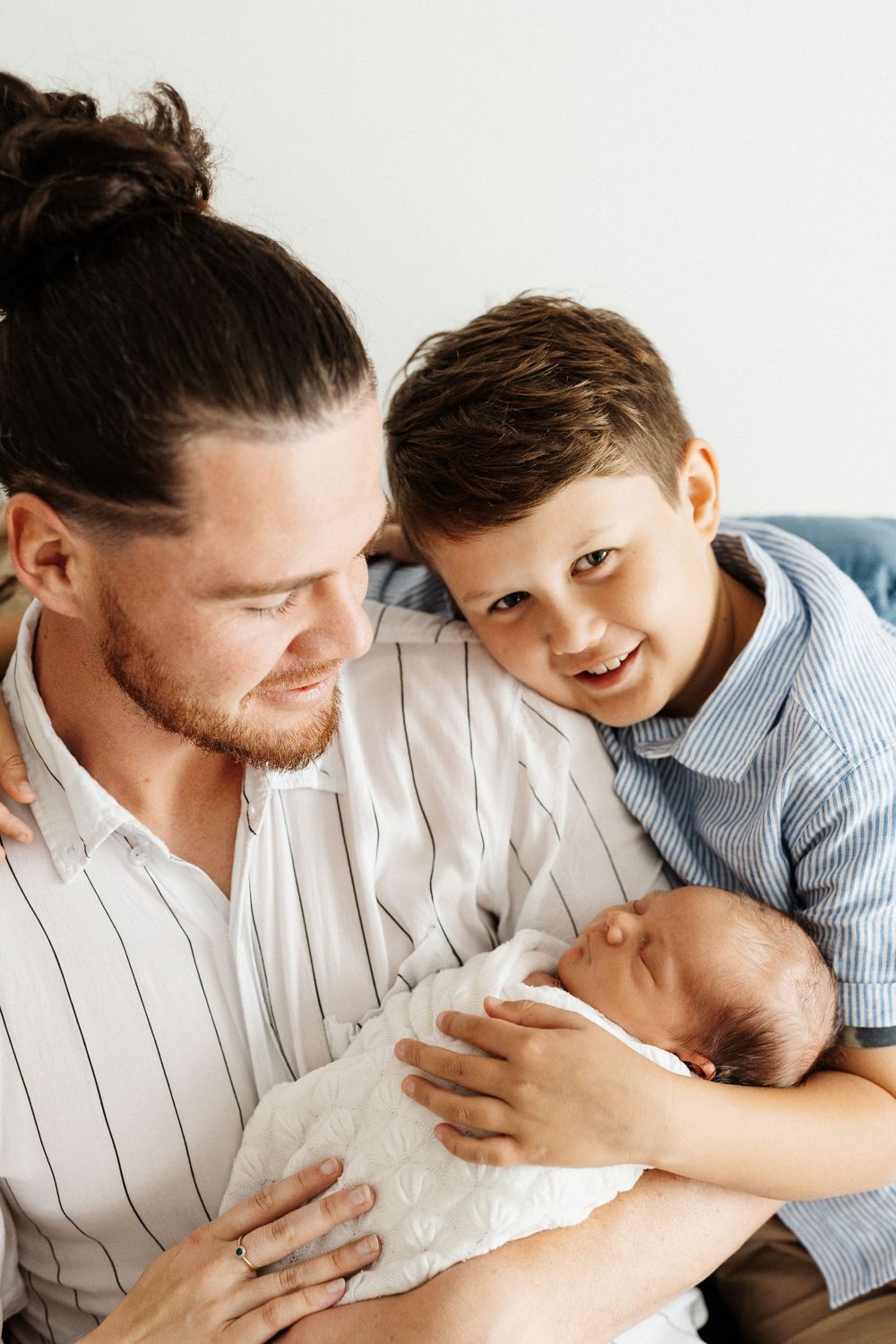 A tender family moment showing a small child and adult looking lovingly at a swaddled newborn.